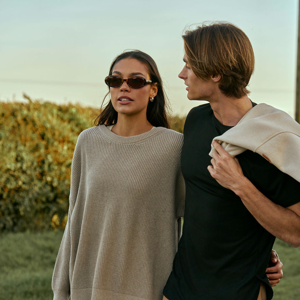 A woman in a grey knitted jumper and sunglasses beside a man holding a cream jumper
