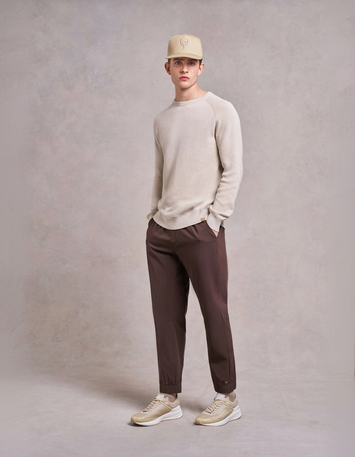 Man in a cream knit, brown trousers and a bucket hat