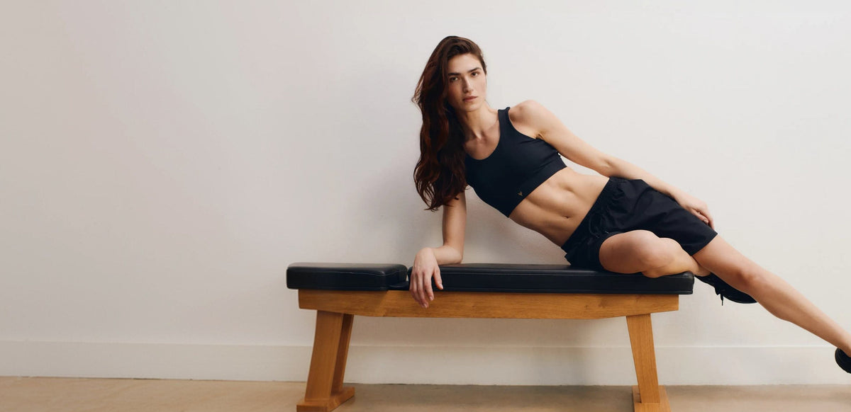 Woman in a black bra top and shorts leaning on a wooden bench
