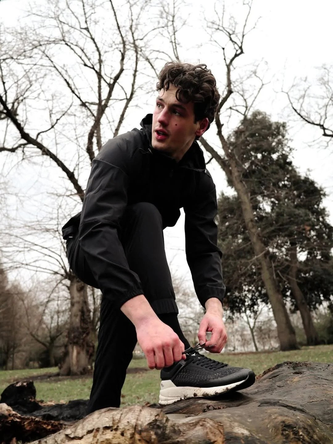 Runner lacing a trainer on a fallen log outdoors