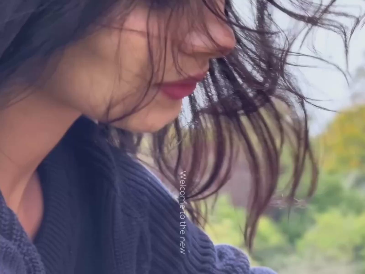 A woman in a navy knitted jumper outdoors, hair in the wind